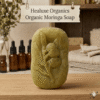 Single oval green organic moringa soap with an elegant leaf design imprint on a wooden surface.