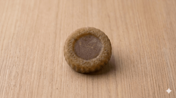 A single round textured gram flour soap bar on a plain wooden background.