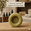 Single round shaped organic moringa soap displayed on a wooden surface with amber serum bottles background.